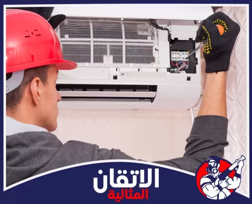 تنظيف المكيفات في الأحساء 0567008659 شركة أتقان المثالية فني مكيفات يرتدي خوذة حمراء وقفازات يضبط الأسلاك الكهربائية في وحدة مكيف سبليت داخلية مفتوحة.