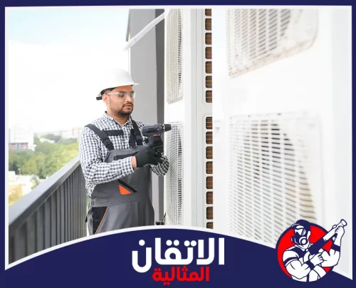 فك المكيفات في الأحساء 0567008659 شركة أتقان المثالية فني صيانة يرتدي خوذة ونظارة واقية، يقوم بإصلاح أو تركيب وحدة مكيف خارجية في الشرفة باستخدام دريل كهربائي.