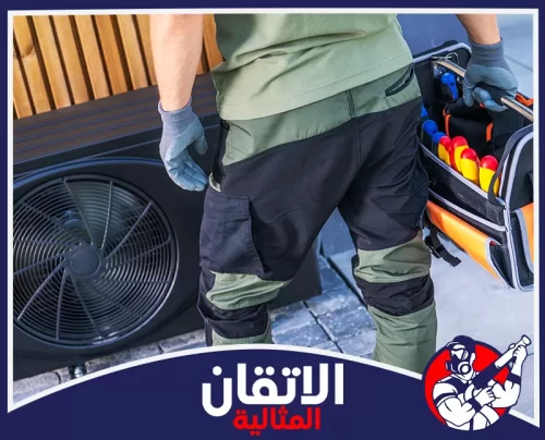 نقل المكيفات في الأحساء 0567008659 شركة أتقان المثالية فني صيانة يرتدي قفازات ويحمل حقيبة أدوات ممتلئة بالمفكات، يقف بجانب وحدة مكيف خارجية سوداء لصيانتها.