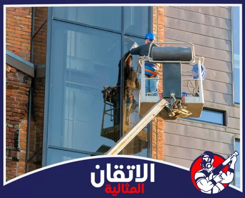 تنظيف سلالم العمائر بالخبر 0567008659 الأتقان المثالية عامل ينظف واجهة زجاجية لمبنى في الخبر باستخدام رافعة مخصصة لضمان لمعان الزجاج ونظافة الواجهة.