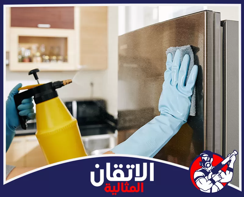 شركة تنظيف مطابخ بالدمام 0567008659 شركة أتقان المثالية شخص يرتدي قفازات زرقاء يمسح ثلاجة ويستخدم بخاخاً أصفر لتنظيف المطبخ