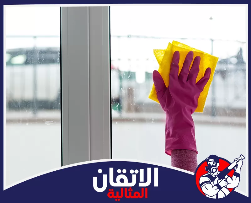 تنظيف زجاج النوافذ من الخارج بالظهران 0567008659 شركة أتقان المثالية يد ترتدي قفازاً وردياً وتمسح زجاج نافذة متسخ بقماش أصفر لإعادة تلميعه ونظافته